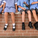 6 Smart Steps: Essential Tips for Buying the Perfect School Shoes. A row of children sitting on a wall displaying their new school shoes.