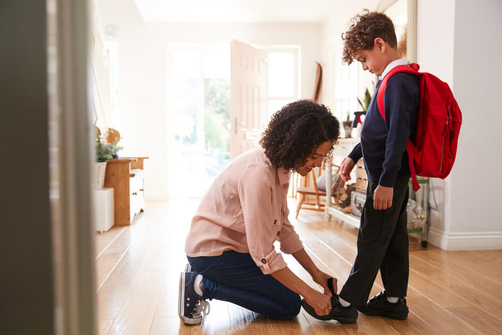 A mum helping to put her son's velcro school shoes on.